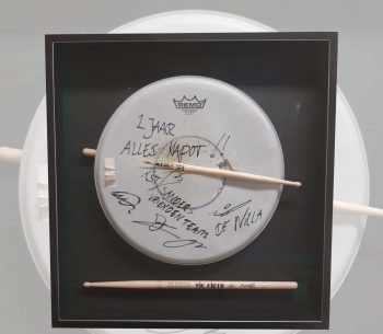 Een gesigneerd drumvel met drumstokken in een verdiepte 3D-lijst