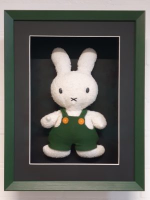 Een goedbewaarde nijntje-knuffel in een groene verdiepte lijst achter glas