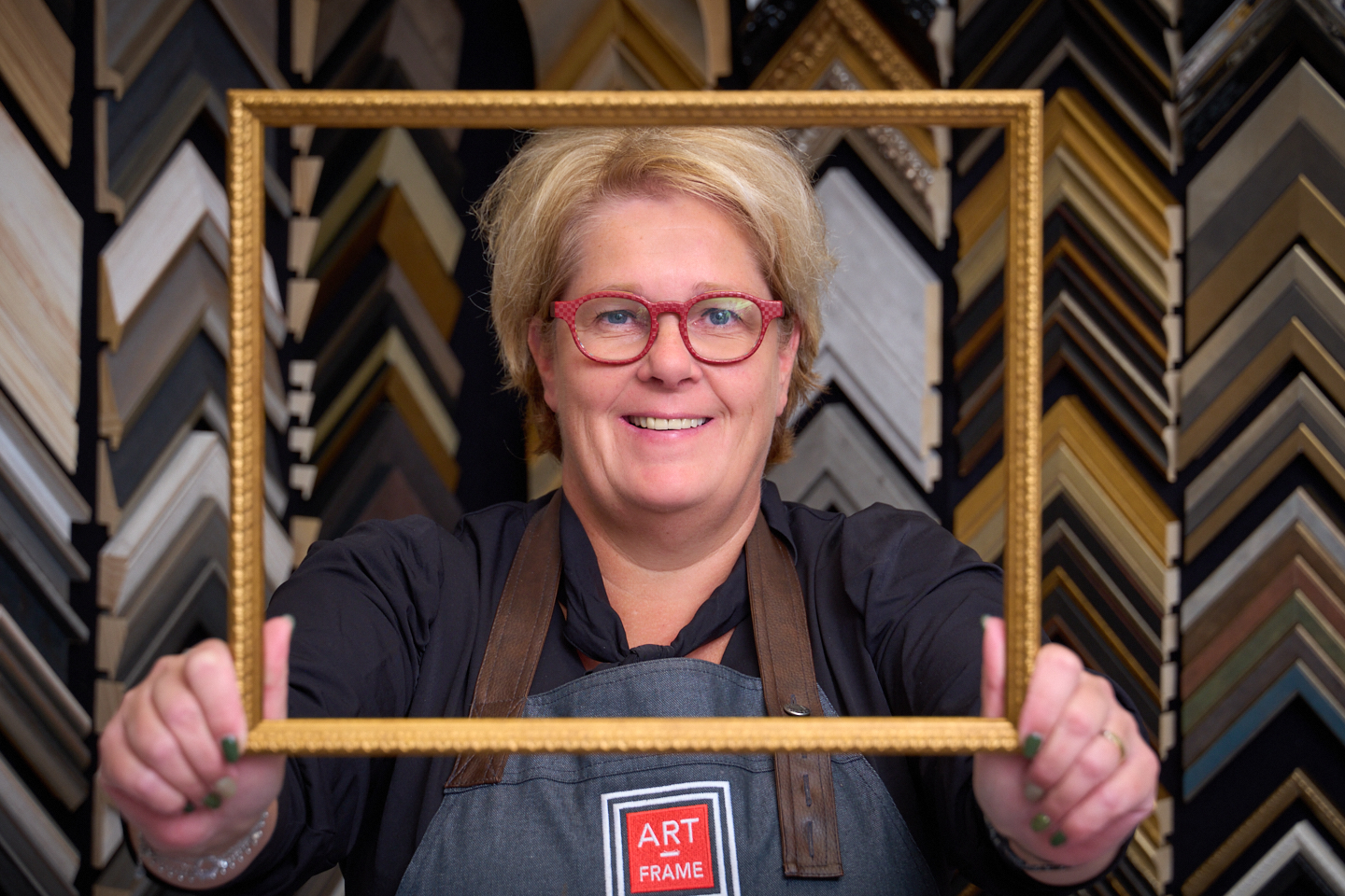 Natascha Heijnen houdt een vergulde lijst omhoog voor een wand met honderden lijstprofielen in het atelier in Nederweert-Eind